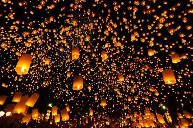 Hundreds of glowing lanterns rising into the night sky during Yi Peng